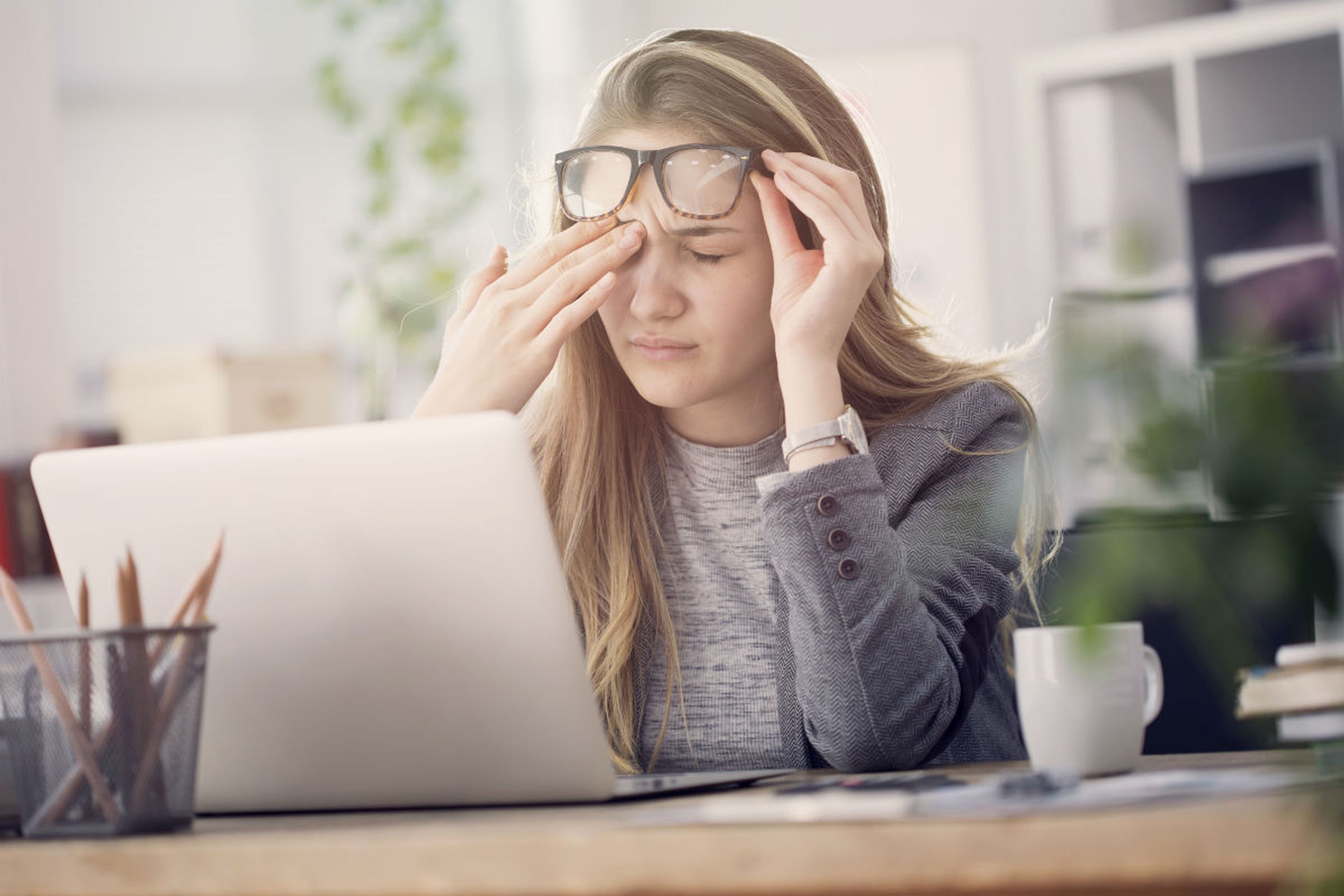 Una mujer se frota los ojos ante su ordenador portátil.