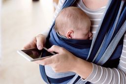 Una mamá que portea a su bebé consulta el móvil