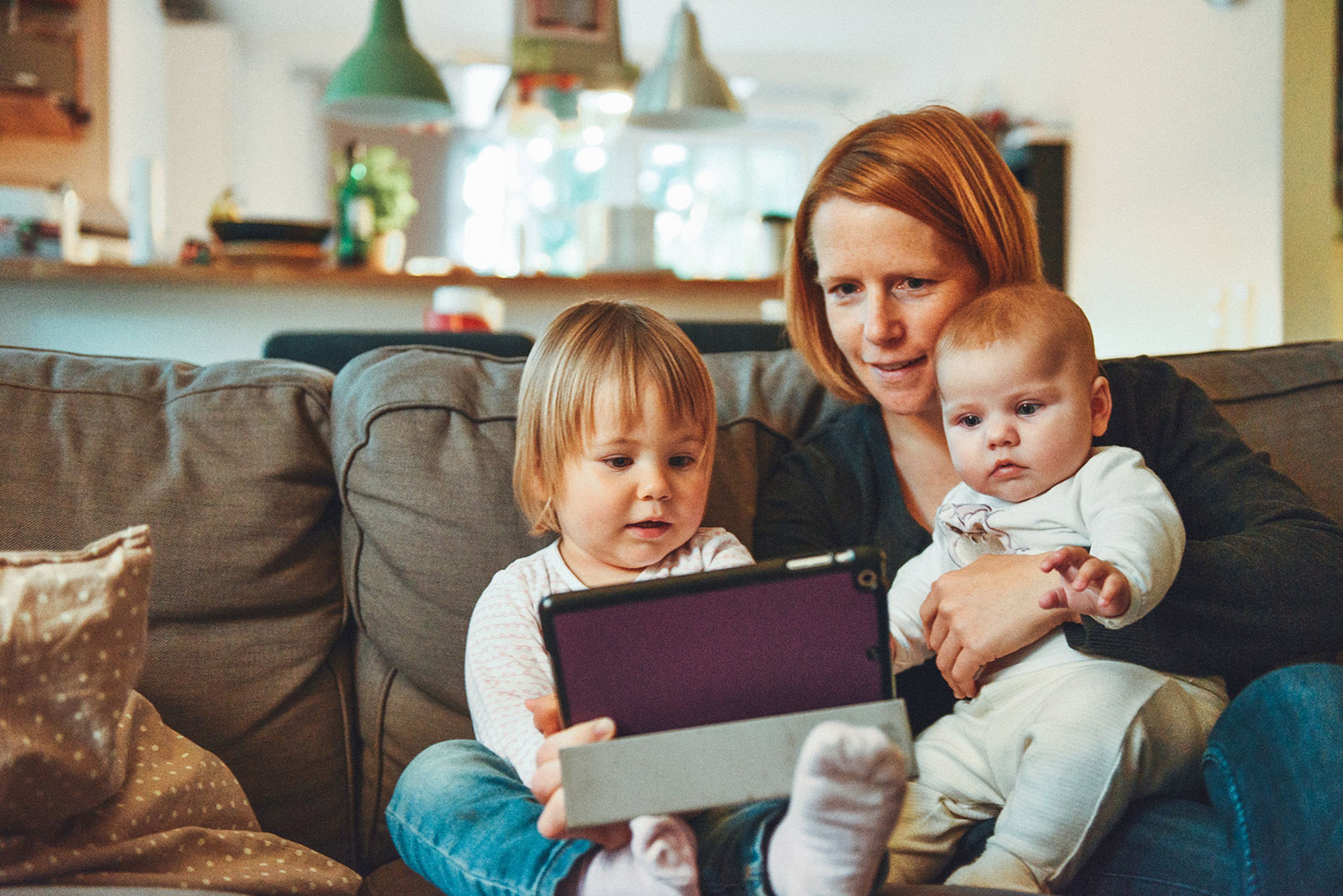 Madre con dos hijos y una tablet en un sofá