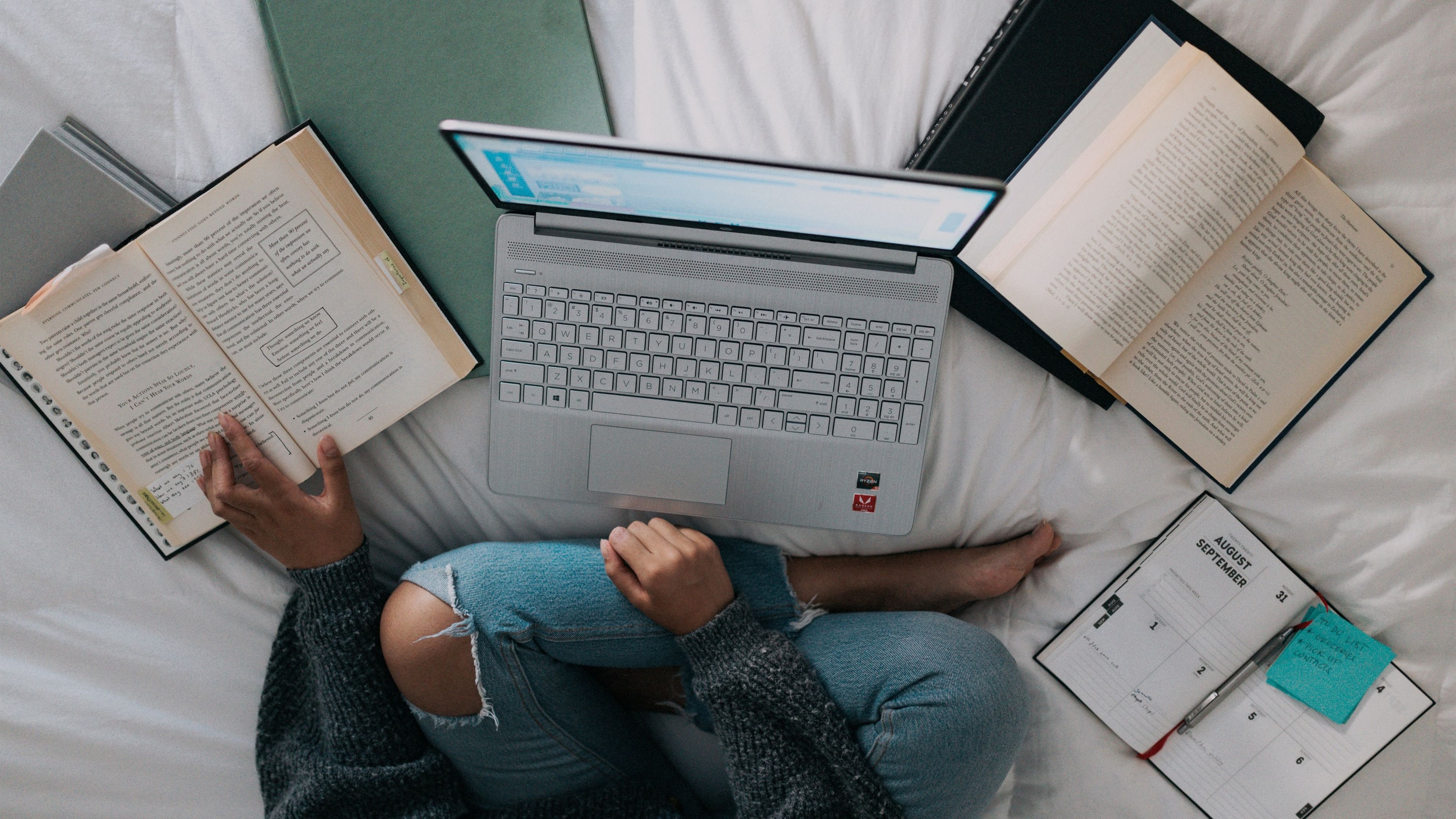 Mujer estudiando con un portátil y libros en una cama