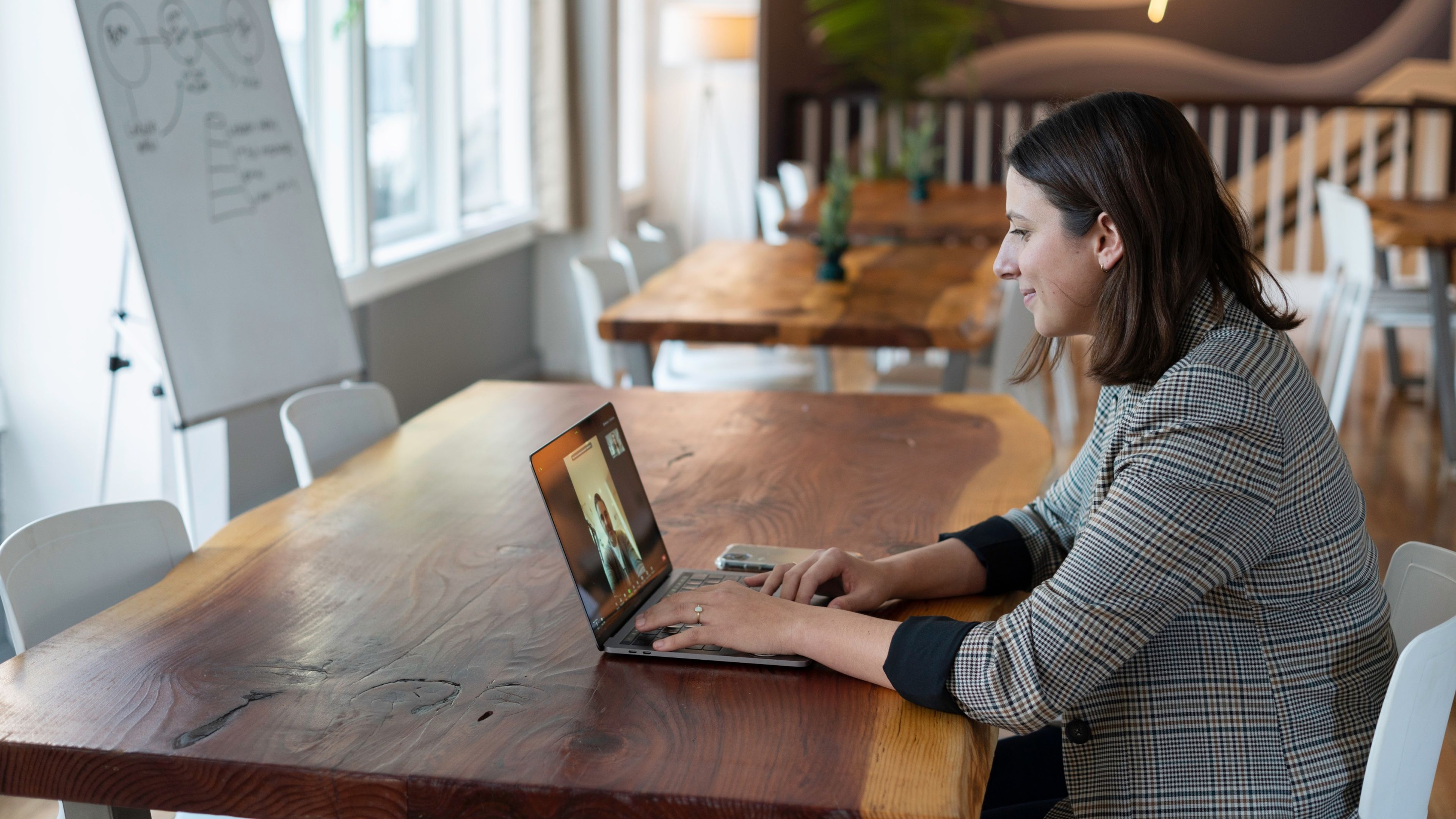 Una mujer atiende a una reunión virtual con su portátil en una zona común de una oficina