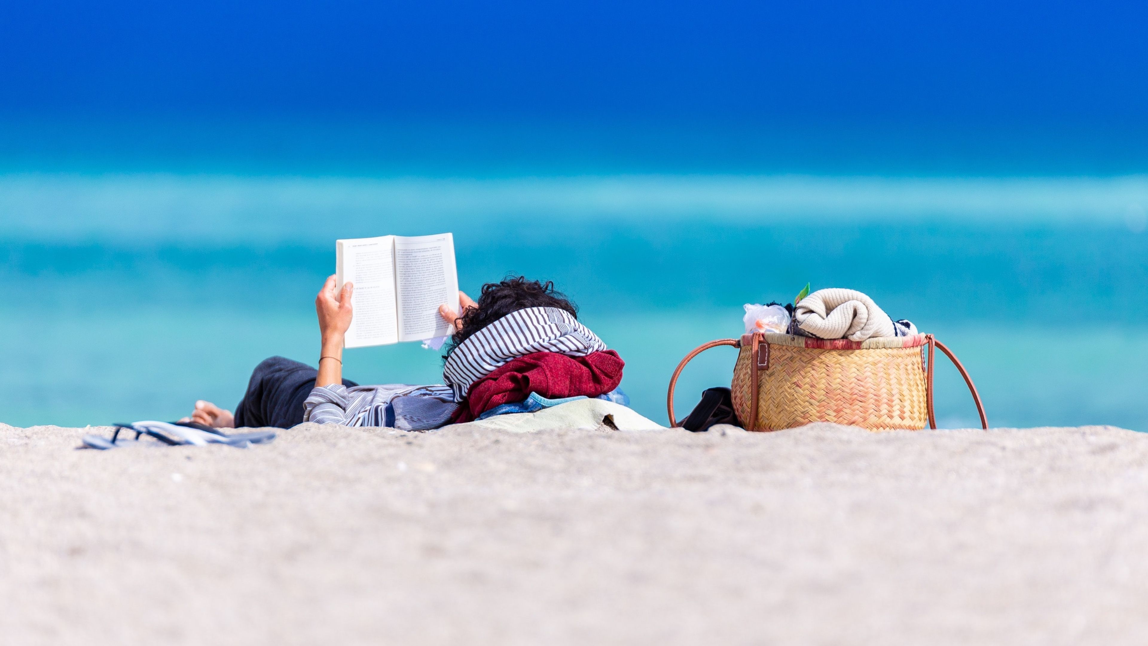 Mujer tumbada en una playa leyendo un libro