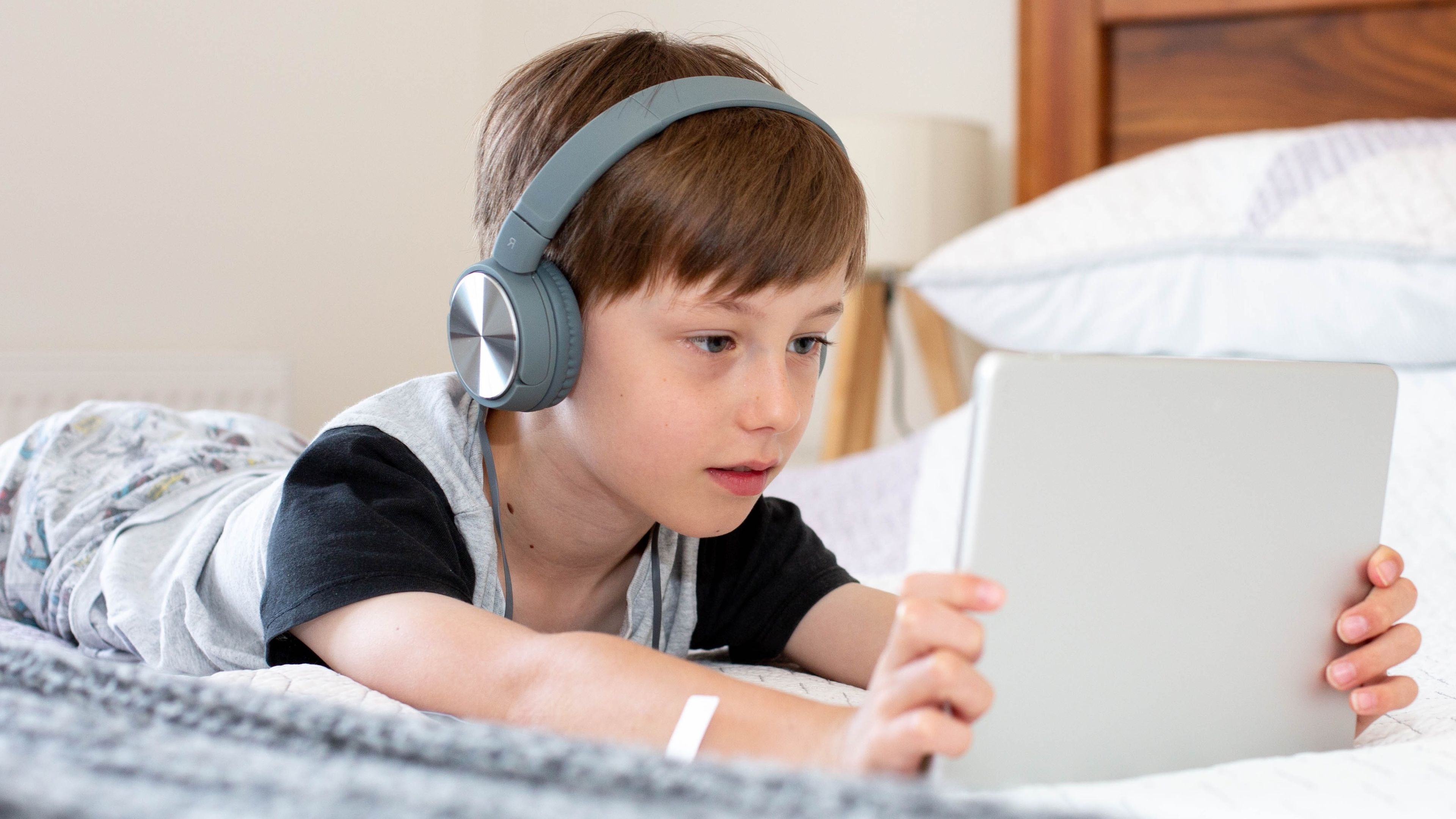Niño en una cama viendo un vídeo en una tablet con auriculares puestos