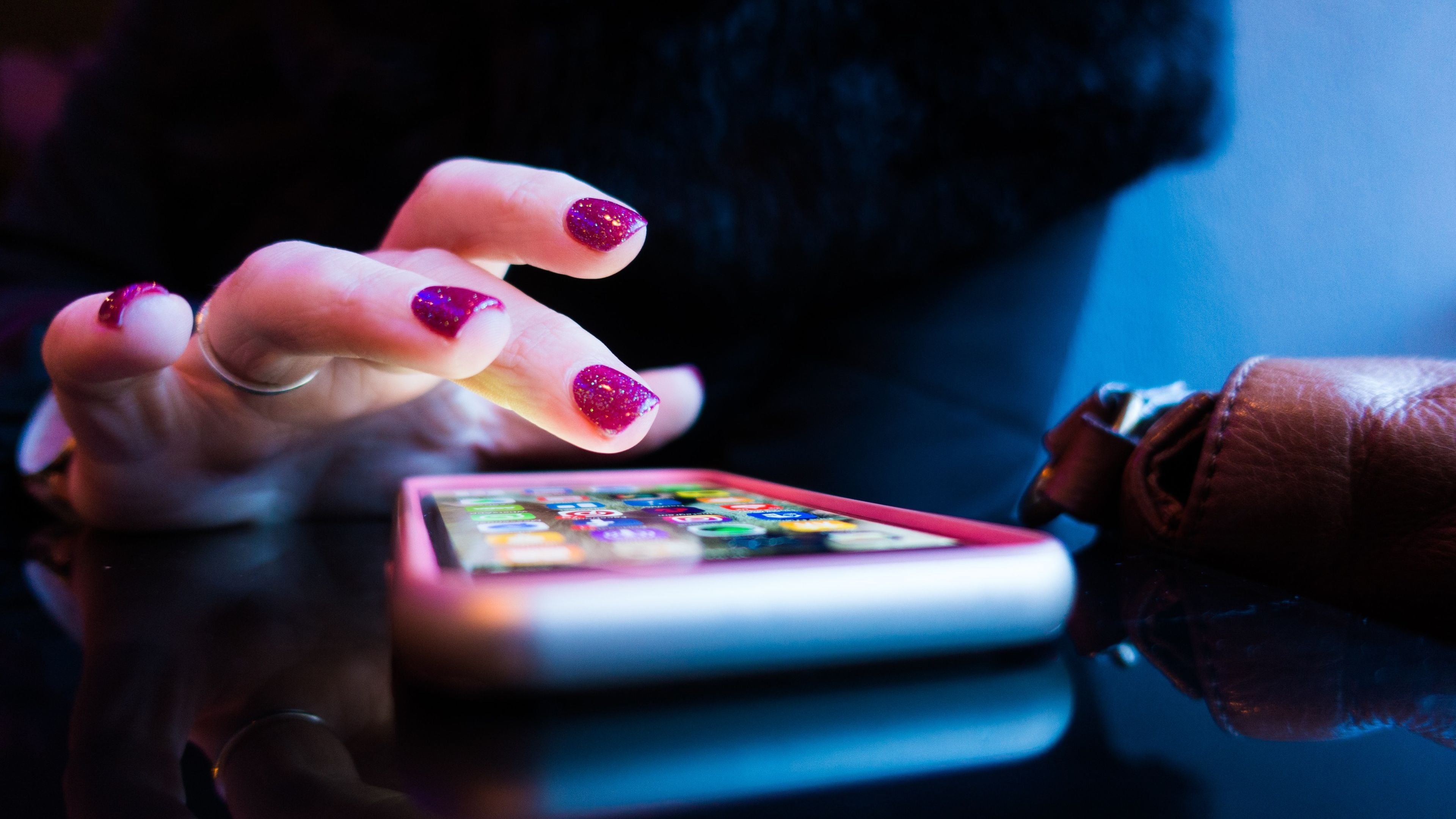 Mujer con las uñas pintadas a punto de abrir una aplicación en un móvil con la pantalla encendida