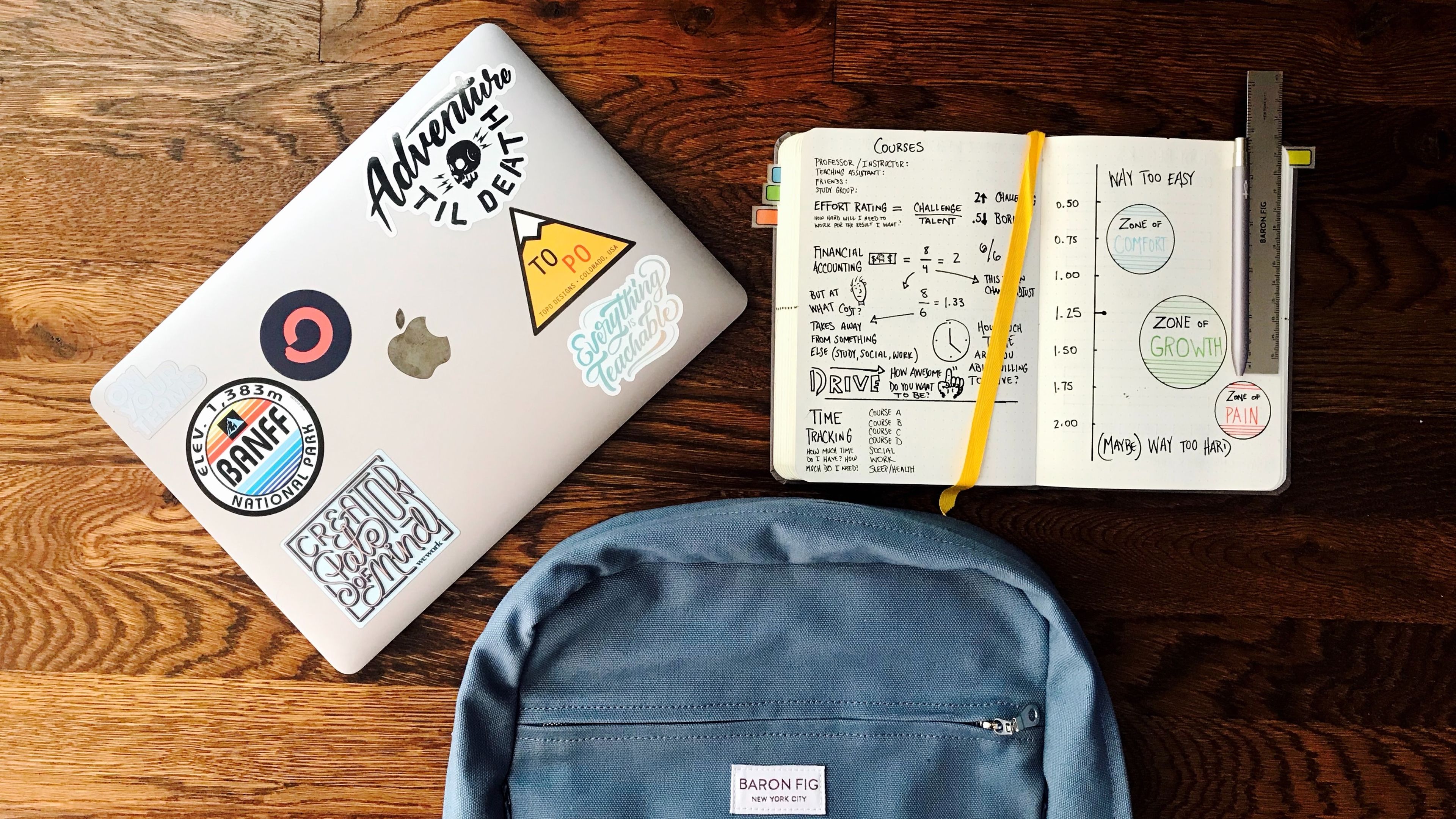 Portátil, cuaderno de notas y mochila posadas sobre una mesa de madera