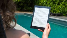 Woman reading an ebook on an ebook reader near a swimming pool