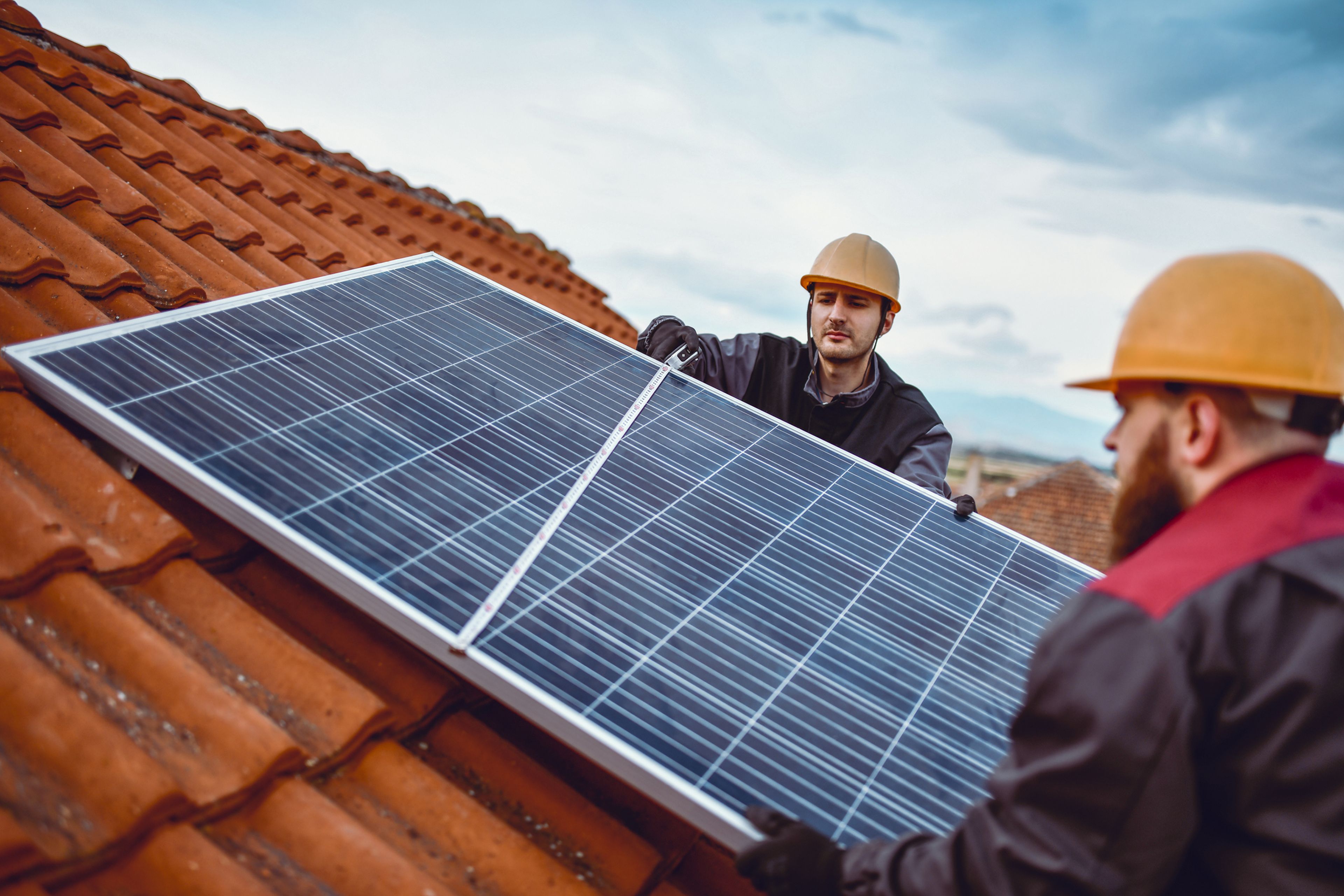 2 personas ponen paneles solares en un tejado.