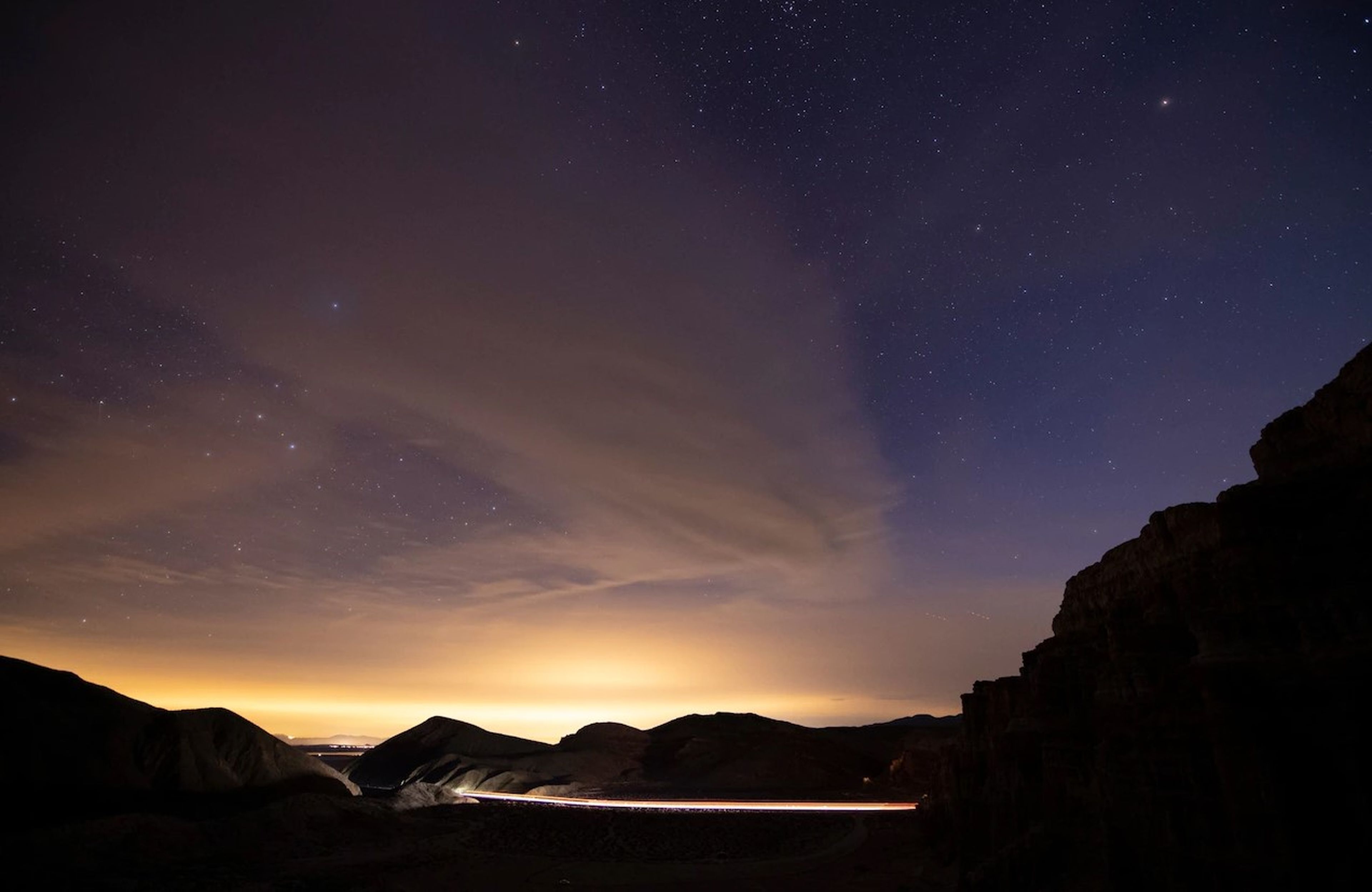 Las luces nocturnas de Los Ángeles son visibles desde una carretera rural. FOTOGRAFÍA DE BABAK TAFRESHI