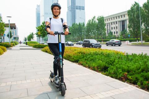 Mujer con casco montada en una scooter eléctrica Mujer con casco montada en una scooter eléctrica